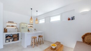 A modern kitchen with white cabinetry, a central island, wooden stools, and pendant lighting.
