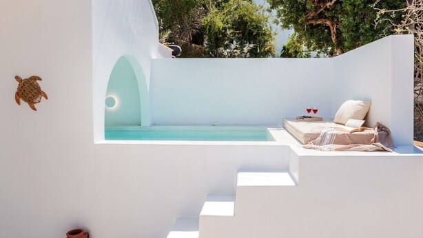 A modern outdoor seating area with a pool, white walls, and a view of trees.