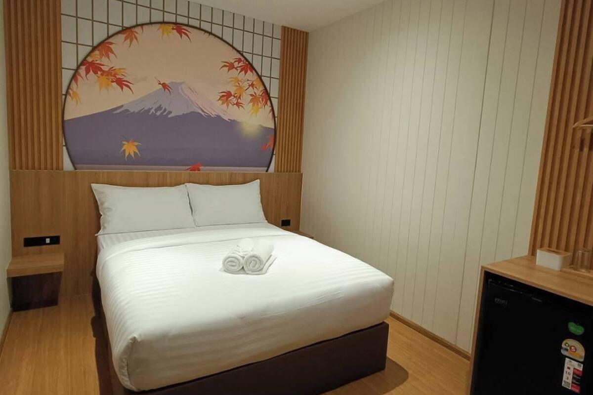 A hotel room with a bed, a small desk, a refrigerator, and a wall with a decorative panel.
