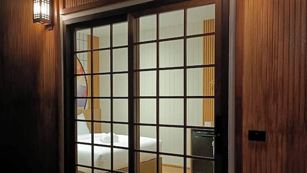 A room with a sliding door, a bed, a small table, and a wall-mounted light fixture. - SK Village (Bangkok)