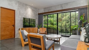Una sala de estar moderna con un ventanal grande, televisor de pantalla plana, muebles de madera y vista a zonas verdes.