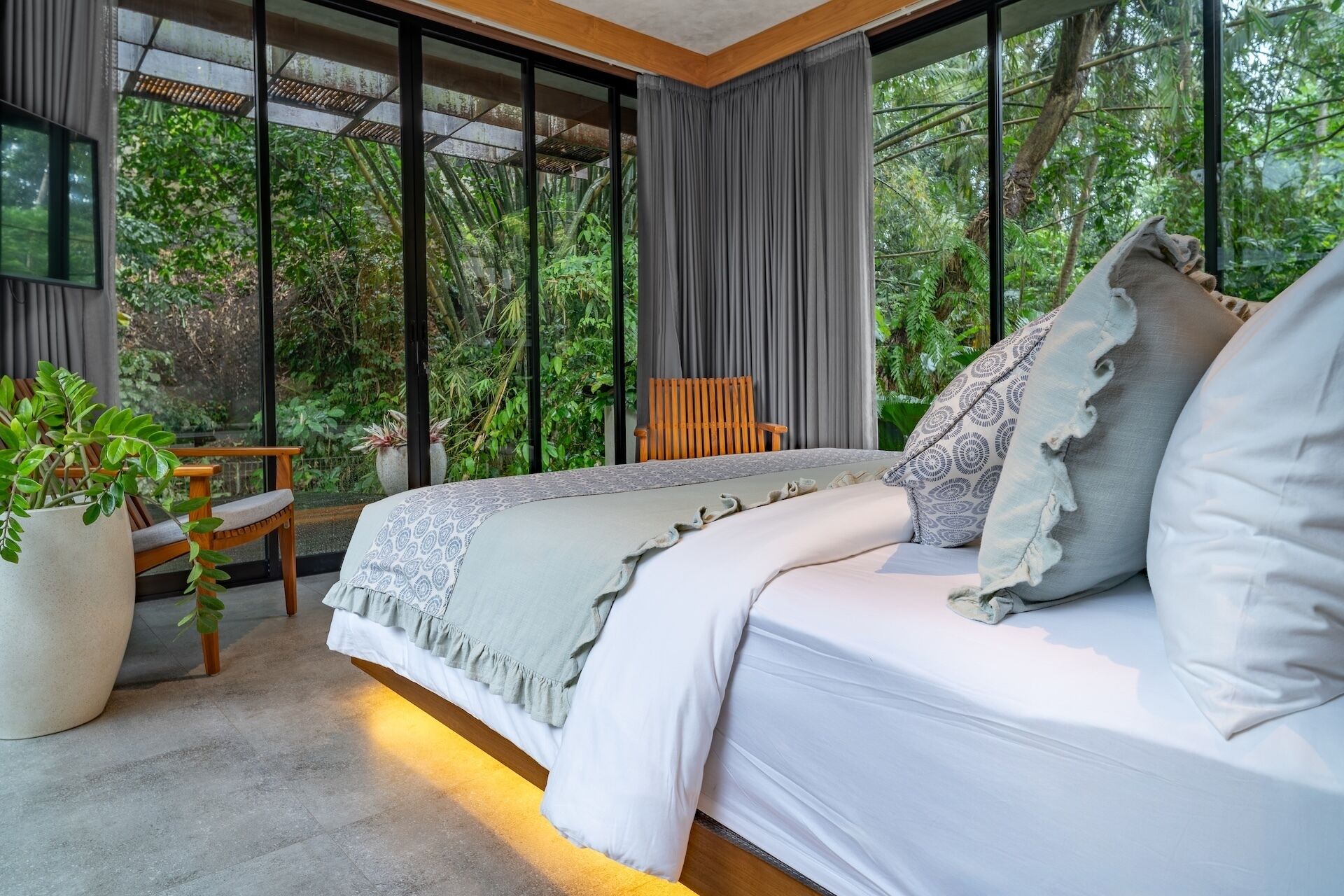 A modern bedroom with a large bed, a wooden chair, and a potted plant.