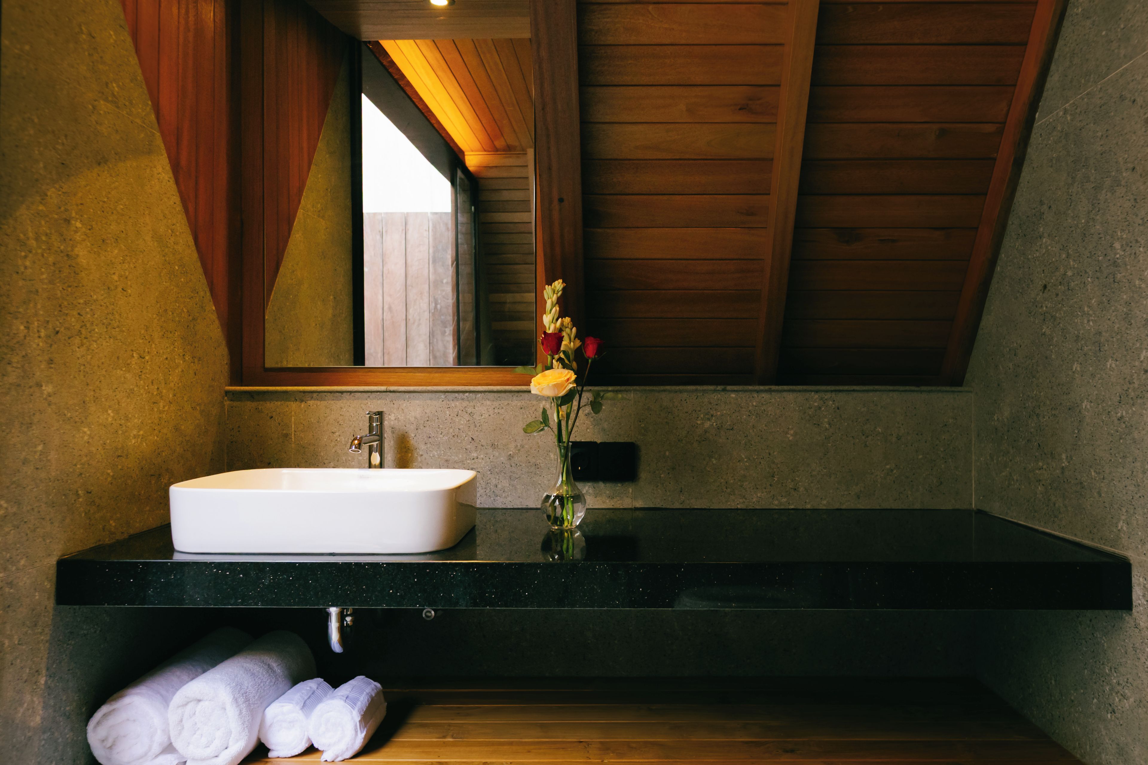 A bathroom with a white sink, a mirror, and a vase with flowers. There are towels on the floor.