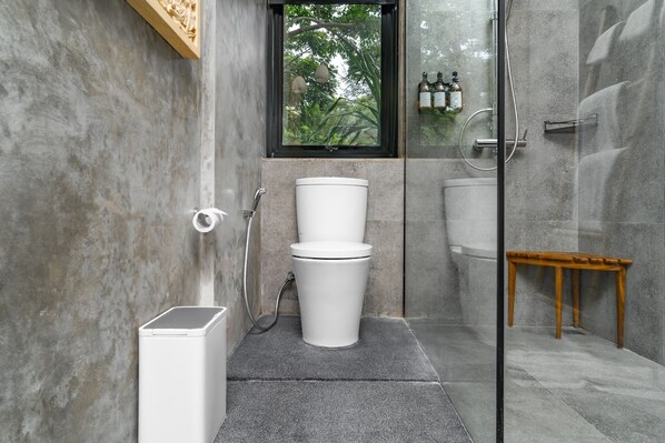 A modern bathroom with a glass shower enclosure, a toilet, and a small wooden bench. - Amarell Ubud Private Luxury Villa (Mas)