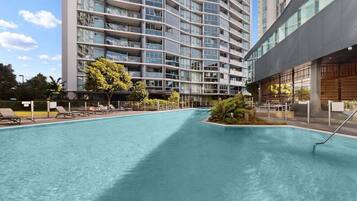 A modern hotel with a large indoor swimming pool, a well-maintained lawn, and a multi-story building with balconies.