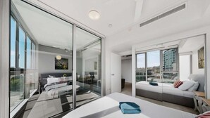 Habitació d'hotel moderna amb un llit gran, un sofà, una partició de vidre i vista a la ciutat.