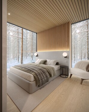 Un dormitorio moderno con una cama grande, una mesita de noche y una silla. Se ve un bosque nevado a través de la ventana.