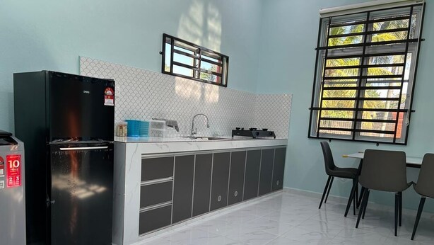 A modern kitchen with a black refrigerator, a sink, and a window with a view of trees. - Homestay Adilah D (Selising)