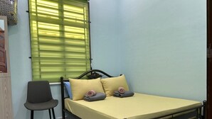 A single bed with a yellow mattress, two pillows, a chair, and a patterned rug in a room with light blue walls and a window with green blinds. - Homestay Adilah D (Selising)