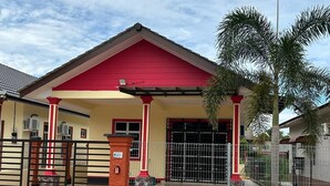 A building with a red and yellow facade, a gated entrance, and a palm tree in front. - Homestay Adilah D (Selising)
