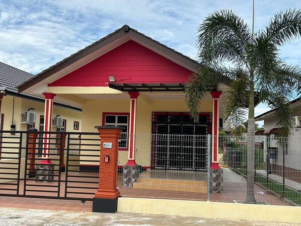 Un edificio con fachada roja y amarilla, un acceso con portones y una palmera al frente.