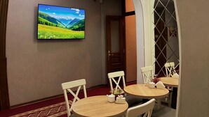 A hotel room with a TV mounted on the wall, a dining area with round tables and chairs, and a decorative ceiling with recessed lighting. - Nizami Boutique Hotel (Baku)