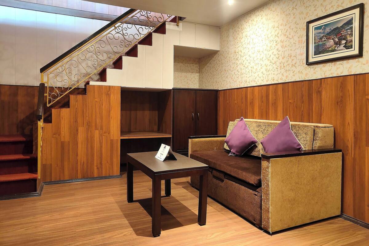 Un escalier en bois avec une rampe en métal, un plancher en bois, un canapé avec des coussins violets et un tableau encadré au mur.