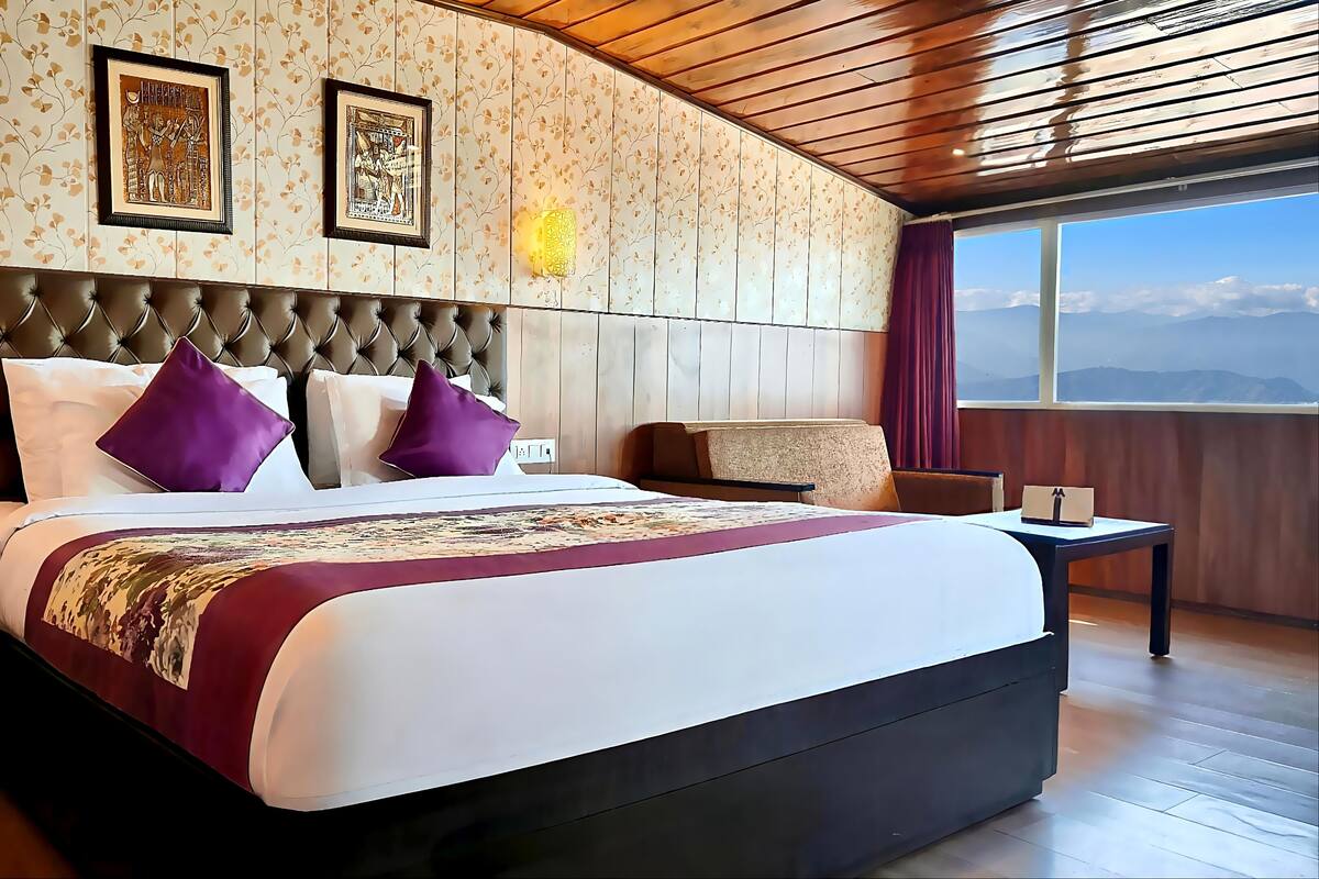 Une chambre spacieuse avec un grand lit, une tête de lit en bois et une vue sur les montagnes par la fenêtre.