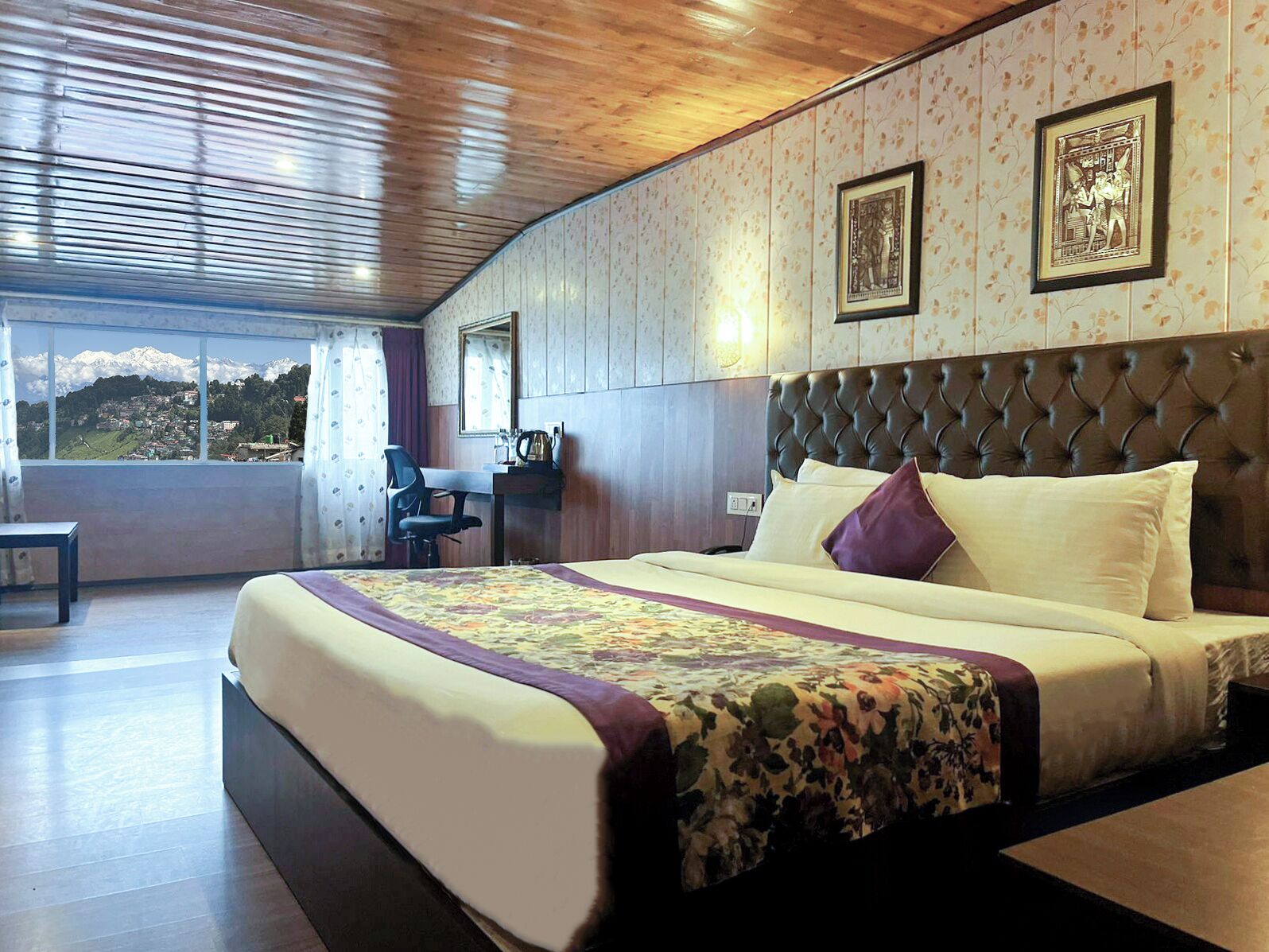 A bedroom with a large bed, a desk, and a chair. There is a window with a view of mountains.