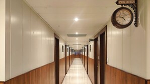Een hotelhal met houten lambrisering, genummerde deuren en een klok die 5:10 aangeeft.