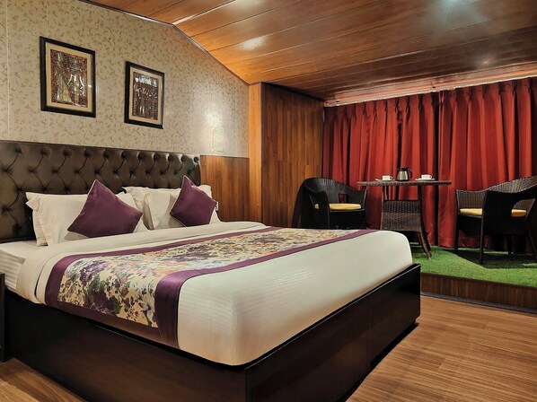 A hotel room with a large bed, a wooden headboard, two framed pictures on the wall, a small table with chairs, and a red curtain. - Valmere Thistle Boutique Hotel (Darjeeling)