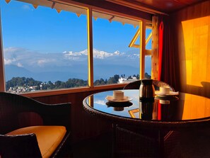 A room with a view of snow-capped mountains and a town. There is a round table with a cup and a thermos. - Valmere Thistle Boutique Hotel (Darjeeling)