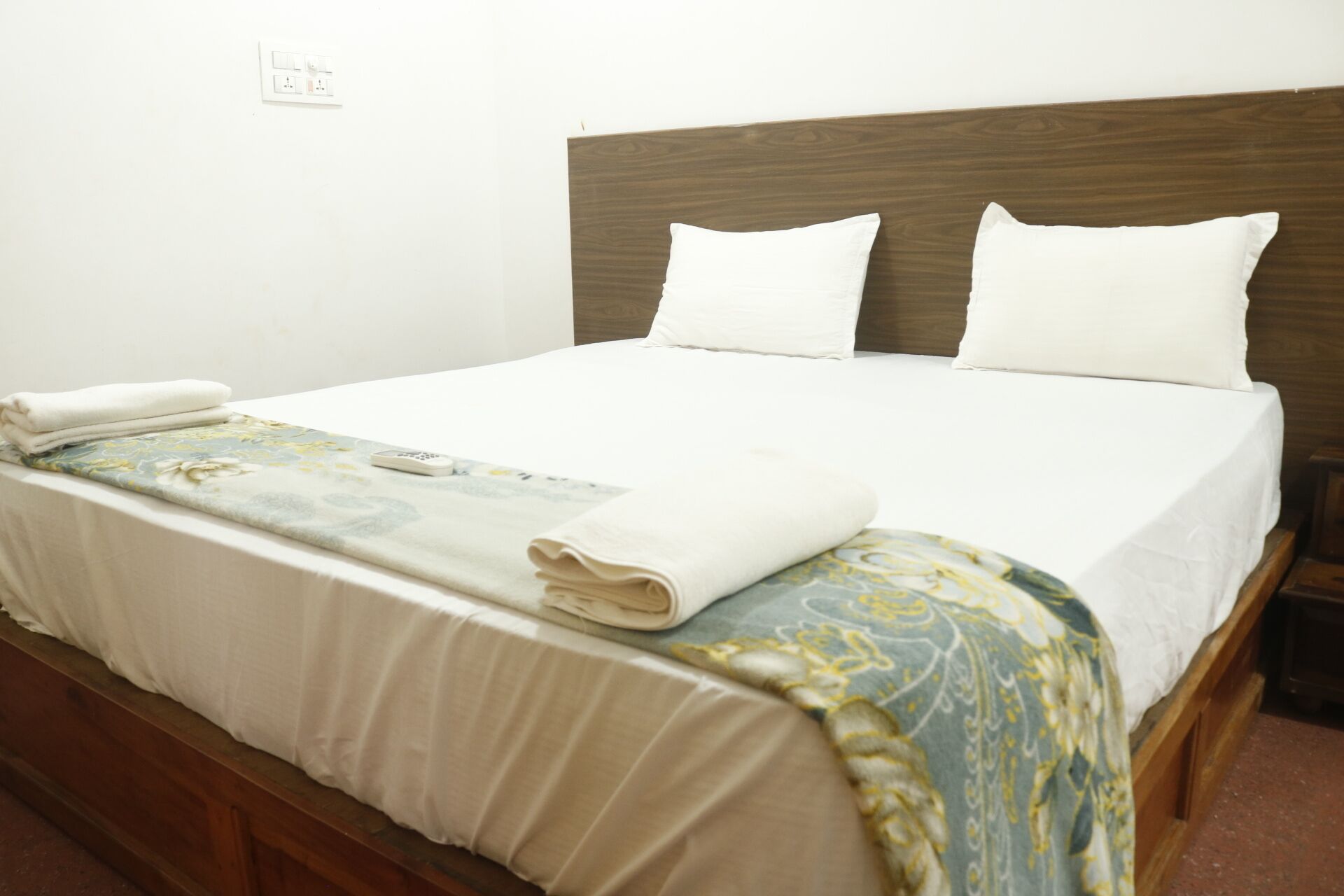 Una cama bien hecha con sábanas blancas, un edredón estampado con motivos florales y dos almohadas.