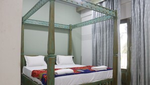 Una cama con dosel con sábanas blancas y una manta colorida, un suelo de madera con un diseño geométrico y una ventana con cortinas grises.