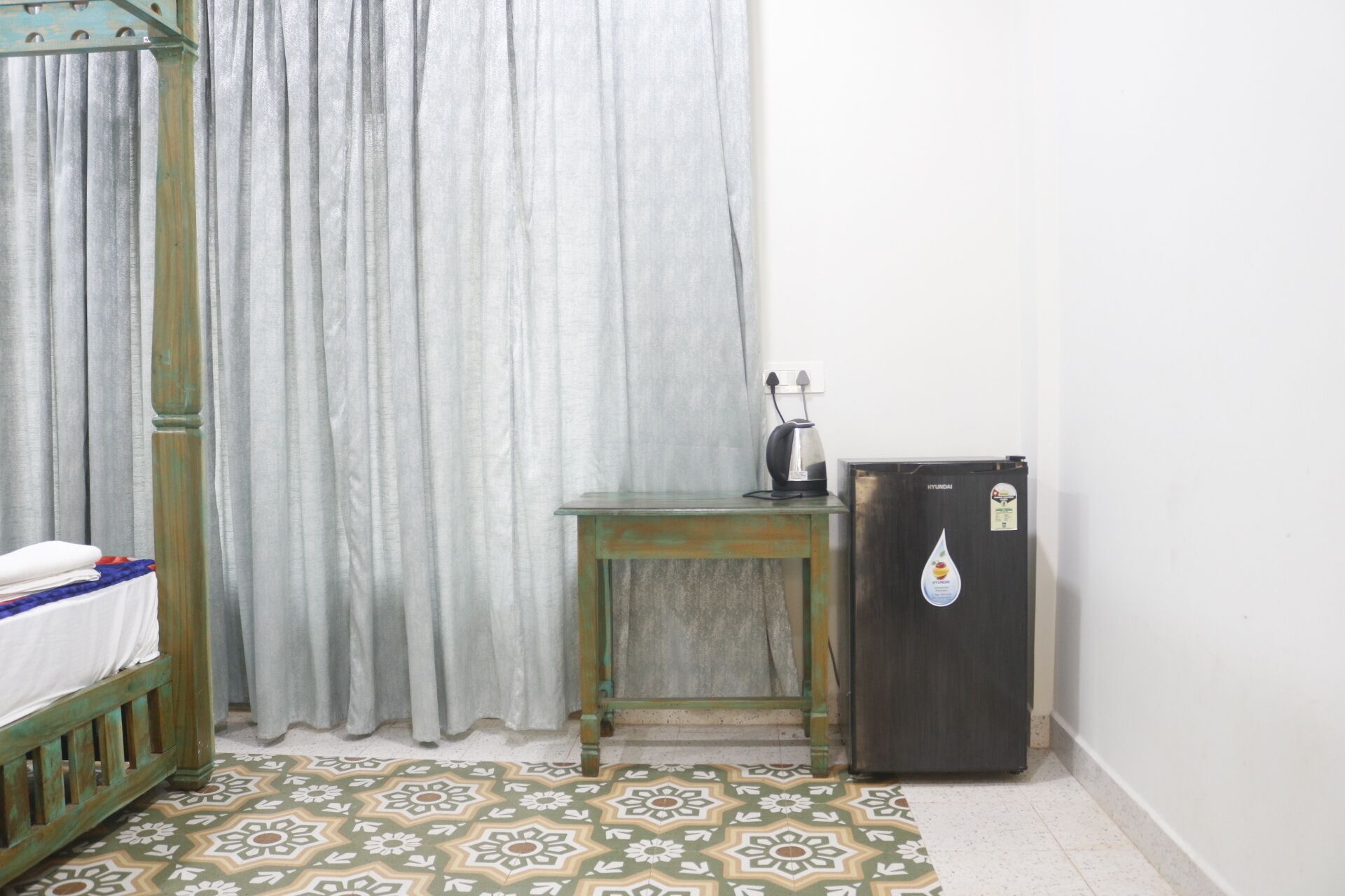 Une pièce comprenant un lit, une petite table, un réfrigérateur et un rideau.