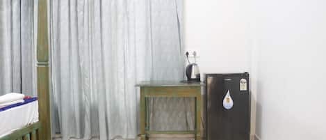 Une pièce comprenant un lit, une petite table, un réfrigérateur et un rideau.