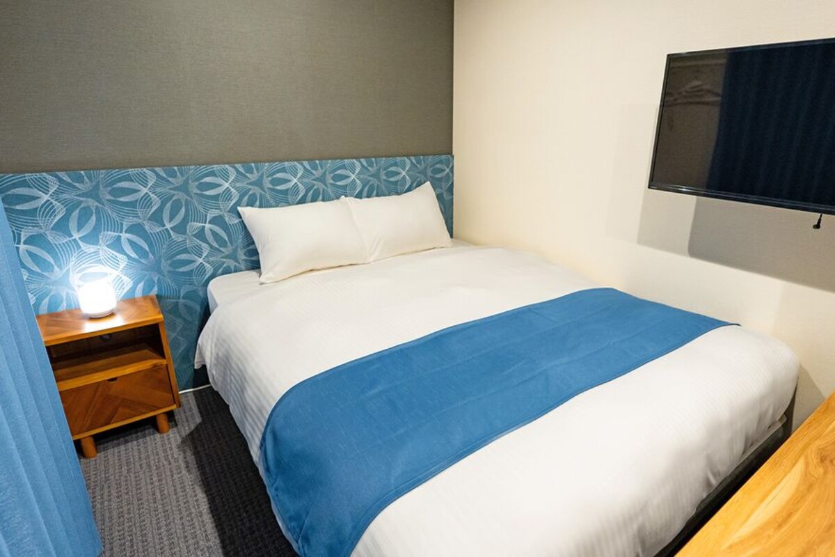 A hotel room with a bed, a nightstand, a TV, and a wooden side table.