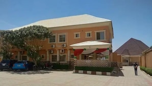 A building with a tiled roof, a covered outdoor seating area, and a paved courtyard. - Gold Rhino Hotel (Enugu)