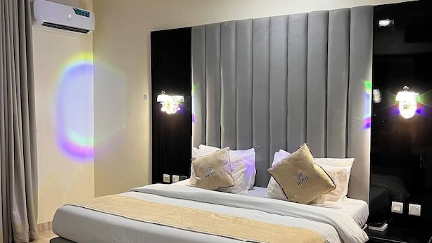 A modern hotel room with a large bed, a bedside table, and a headboard with built-in lighting. - Gold Rhino Hotel (Enugu)