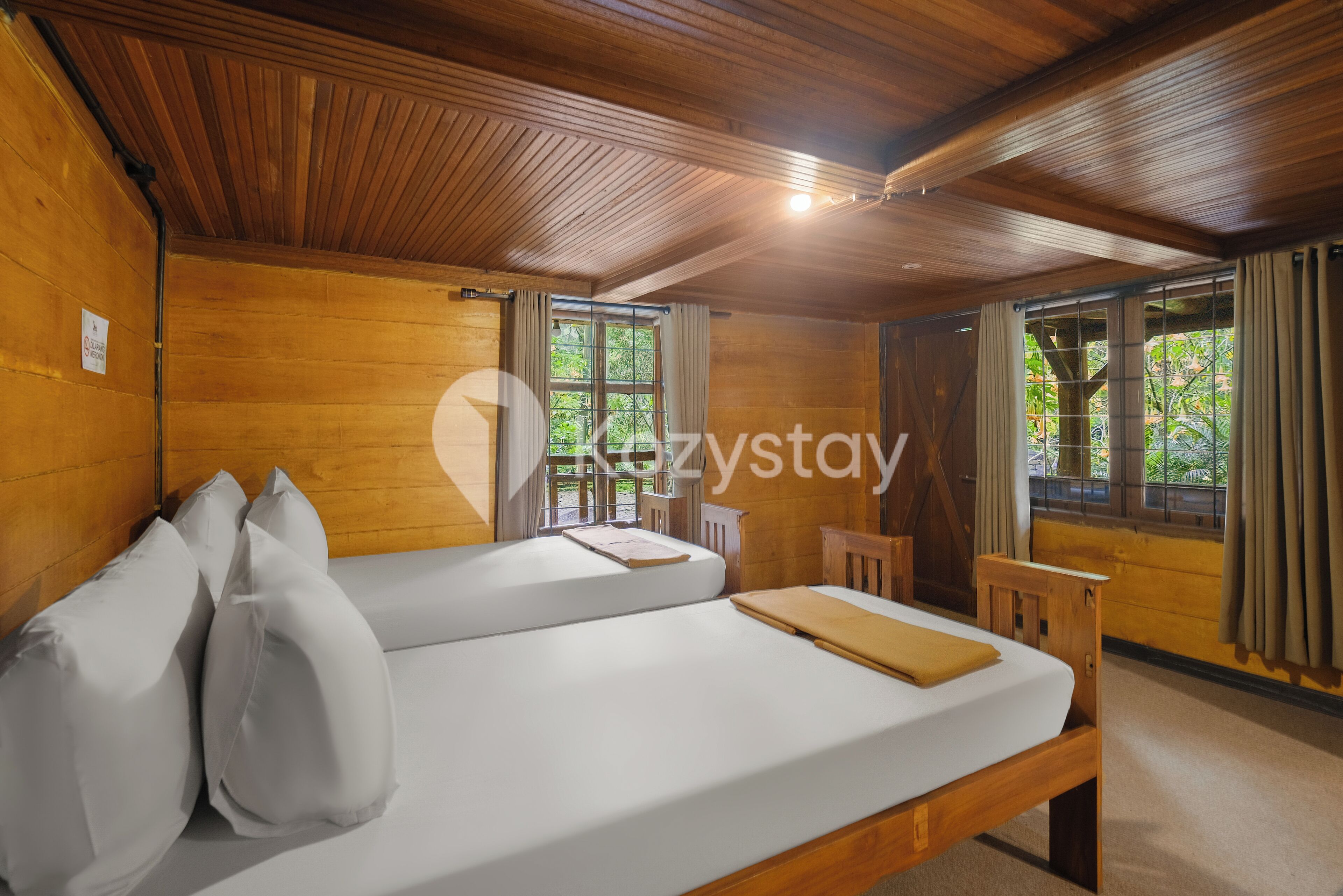 Una habitación de cabaña de madera con dos camas, una mesita pequeña y ventanas amplias.