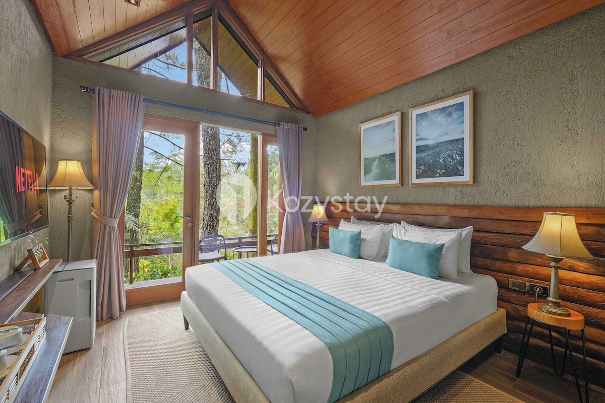 A hotel room with a large bed, a TV, a desk, and a window with curtains.