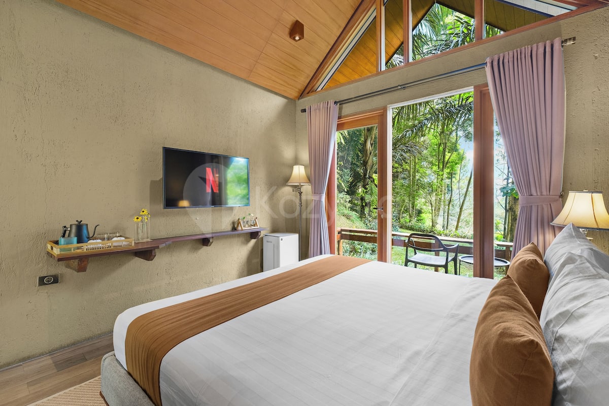 A bedroom with a bed, a TV, a window with curtains, a small table, and a chair.