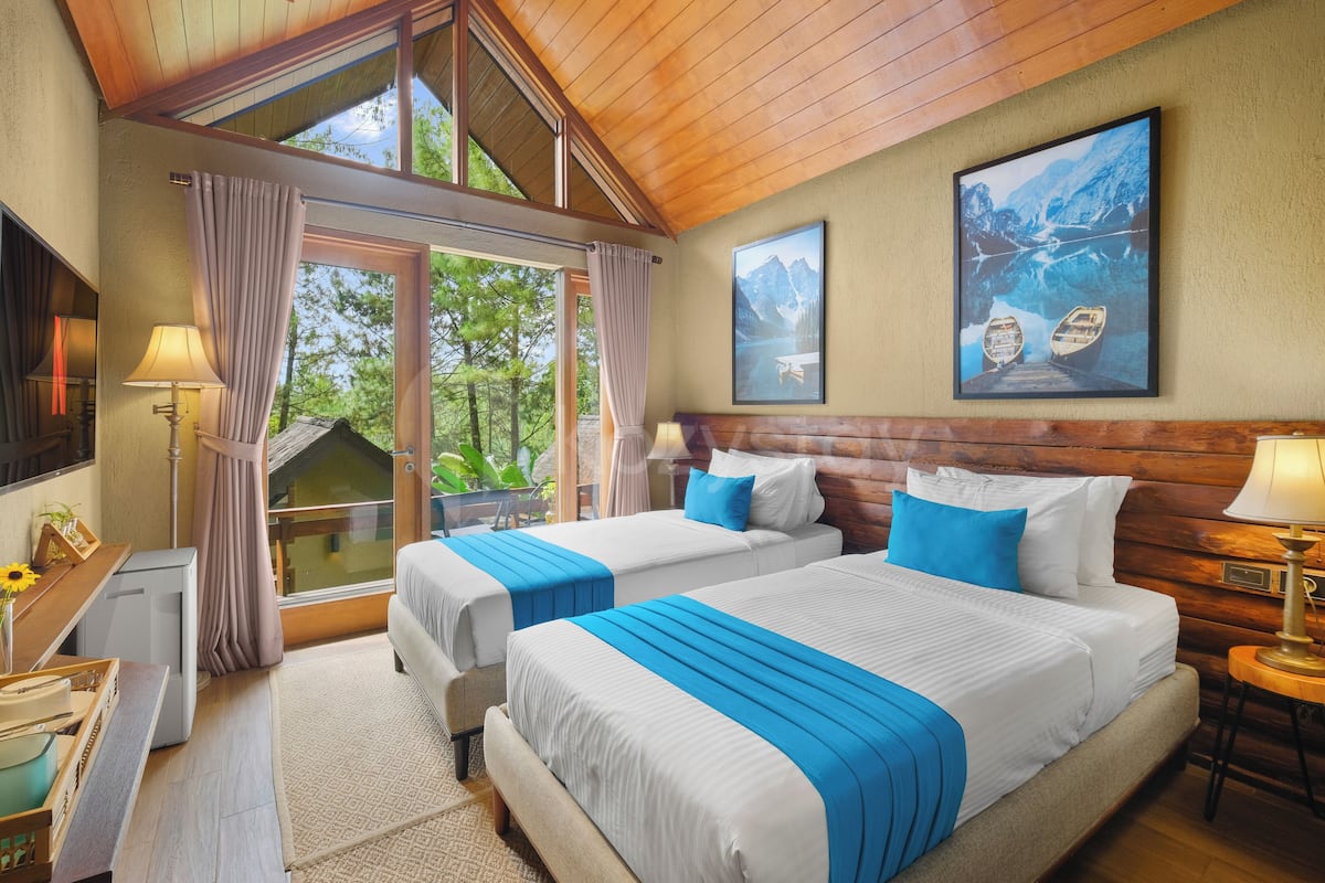A hotel room with two beds, a large window, a painting, and a wooden ceiling.