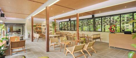 A spacious indoor area with wooden furniture, large windows, and potted plants.