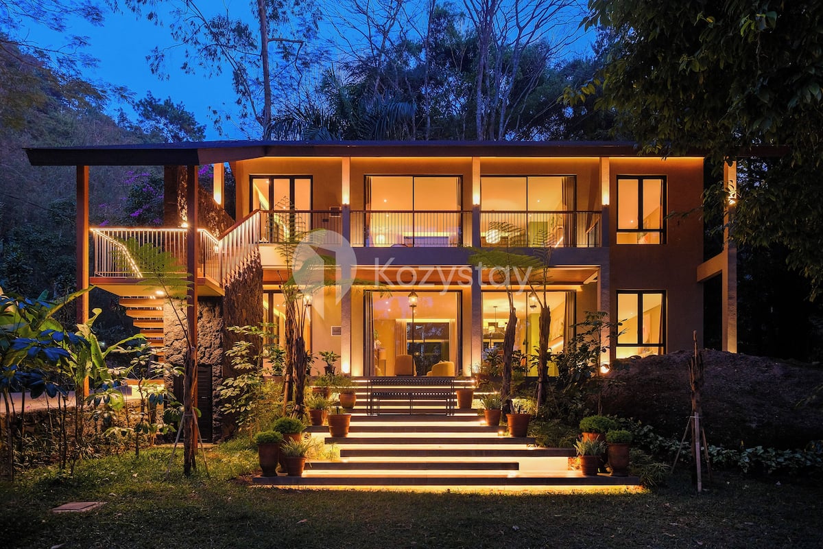 A modern two-story house with a balcony, large windows, and a well-lit entrance.