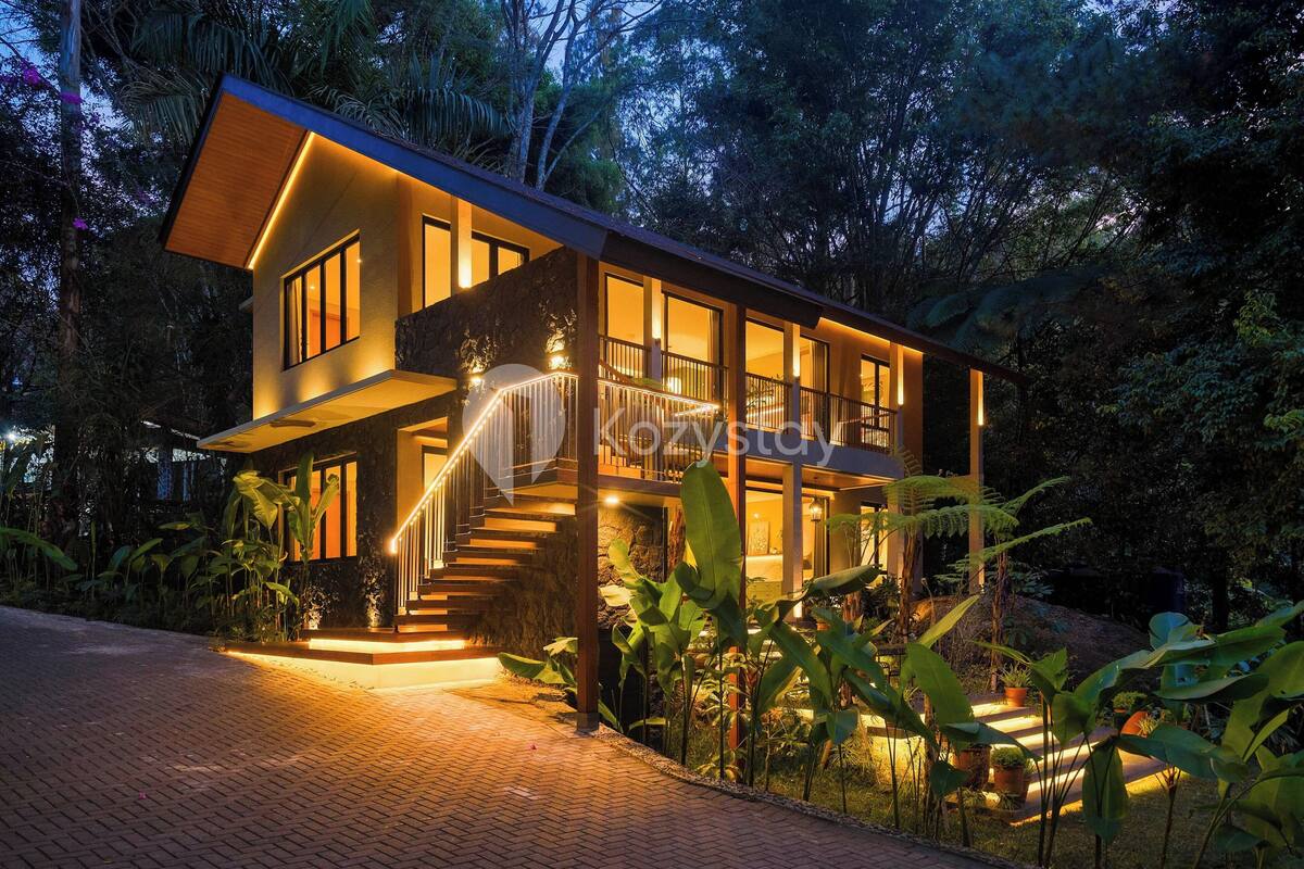 A modern two-story house with a balcony, surrounded by lush greenery.