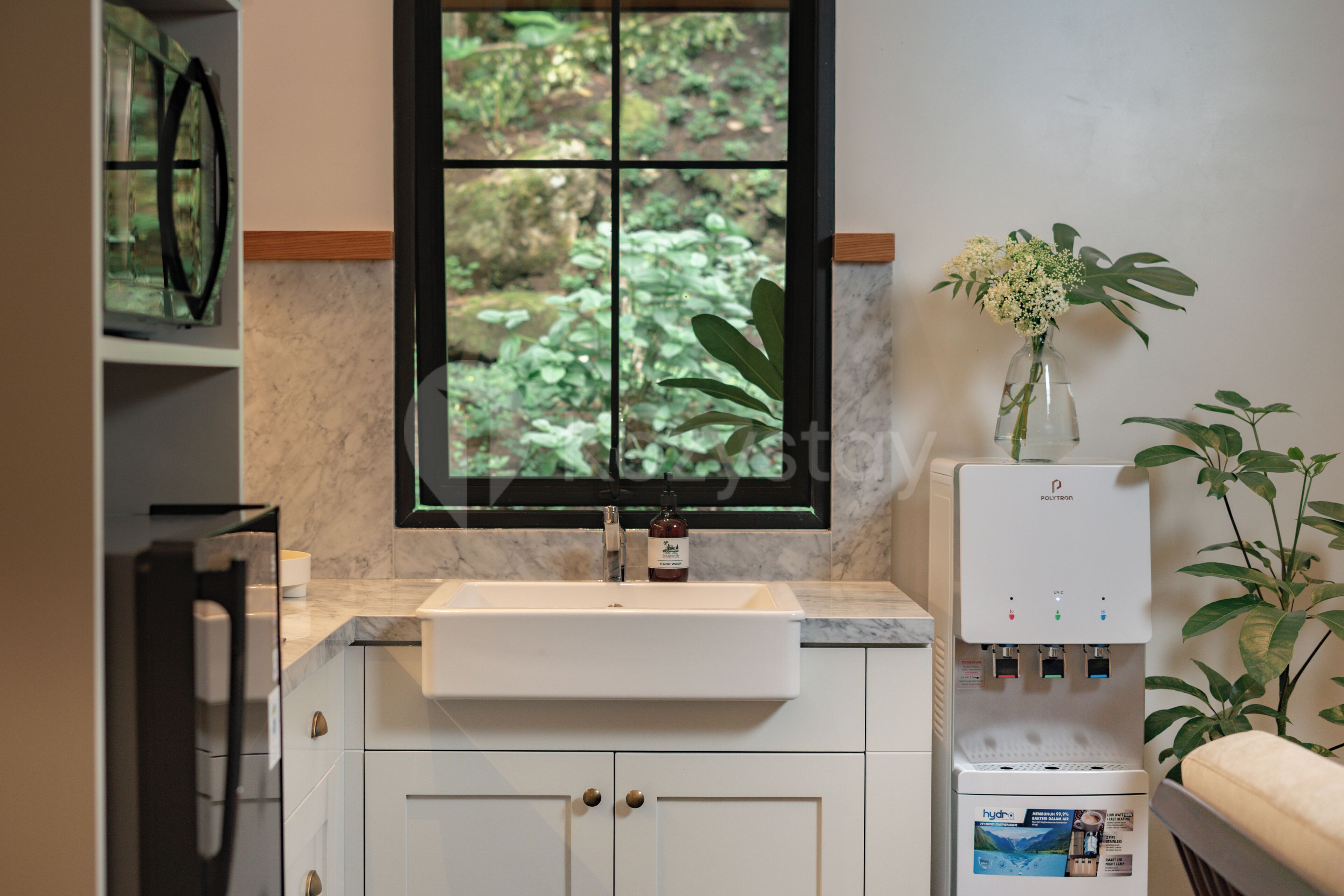 Eine moderne Küche mit Marmorarbeitsplatte, integriertem Spülbecken, einem Fenster mit Blick auf Grünflächen und einem Wasserspender.