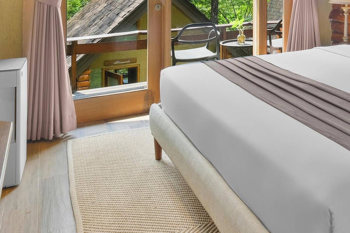 A bed with a headboard, a bedside table with a lamp, and a view of the outdoors.