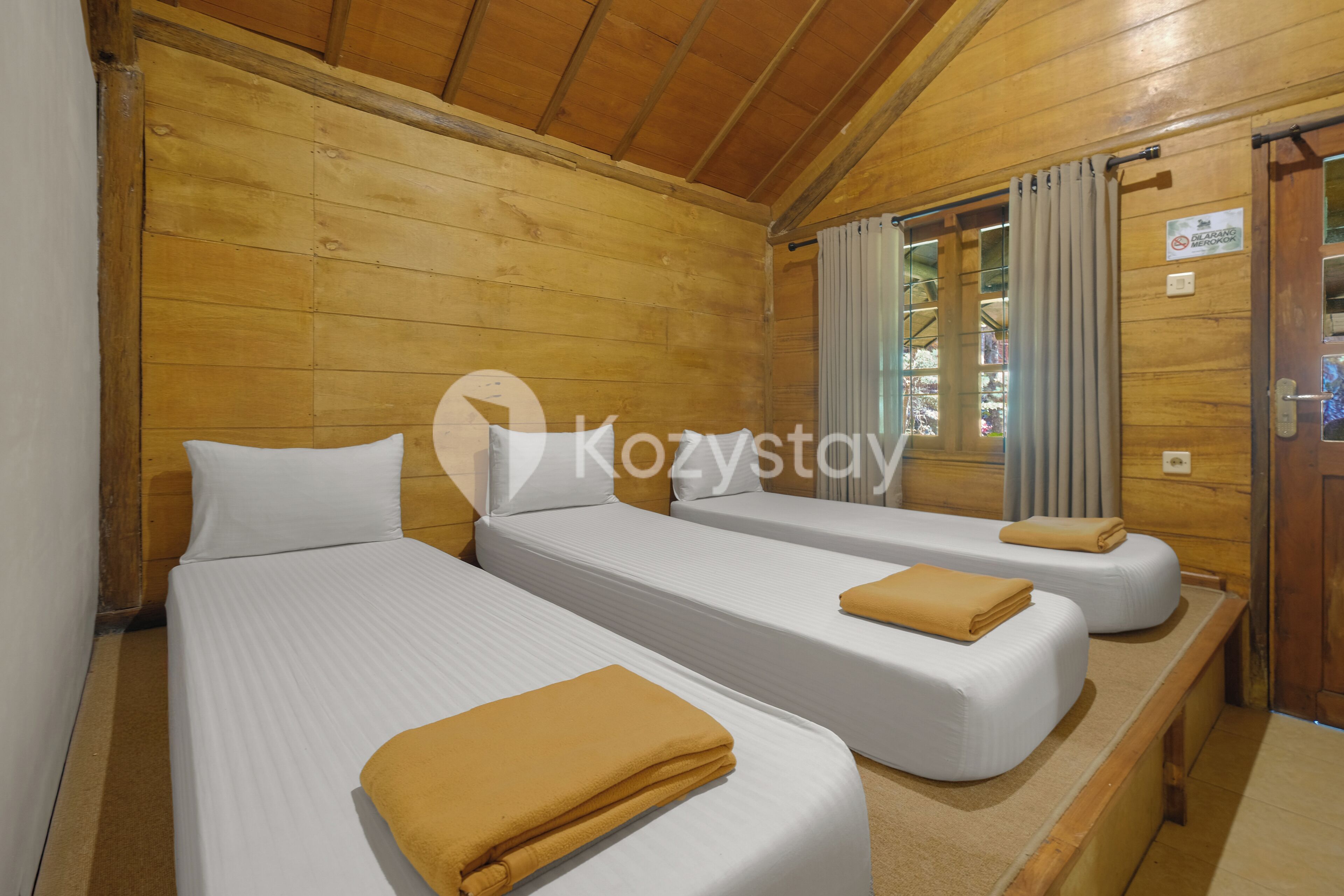 A wooden cabin room with two beds, each with a white mattress and a brown blanket.