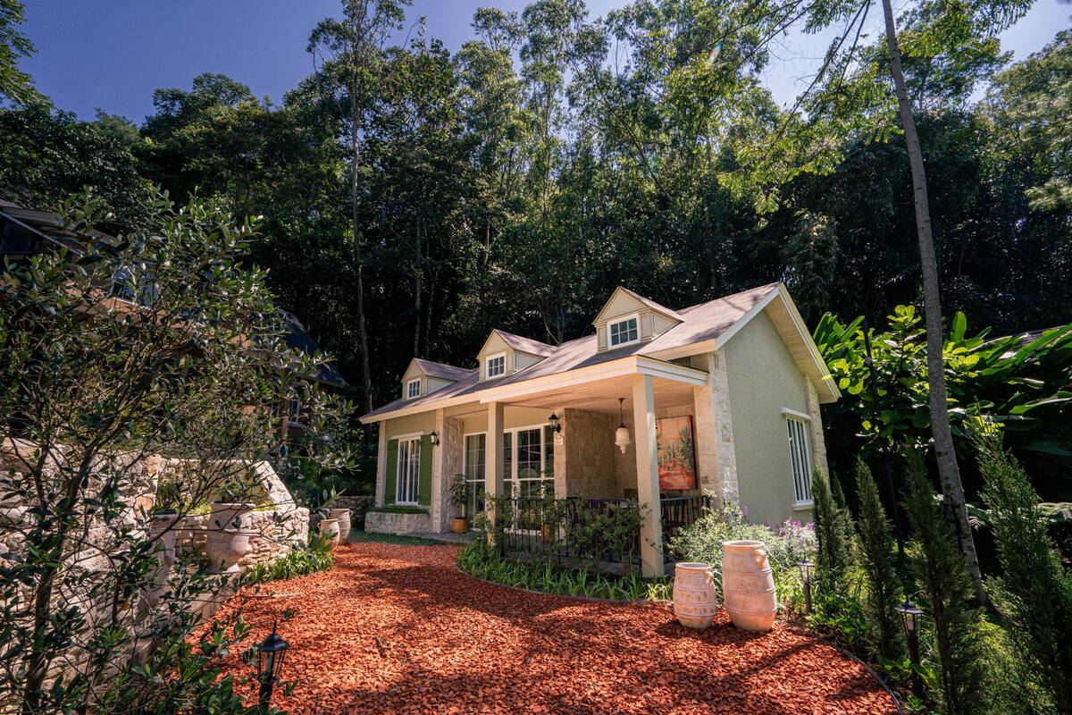 A two-story house with a covered porch, surrounded by dense trees and a red mulch pathway.
