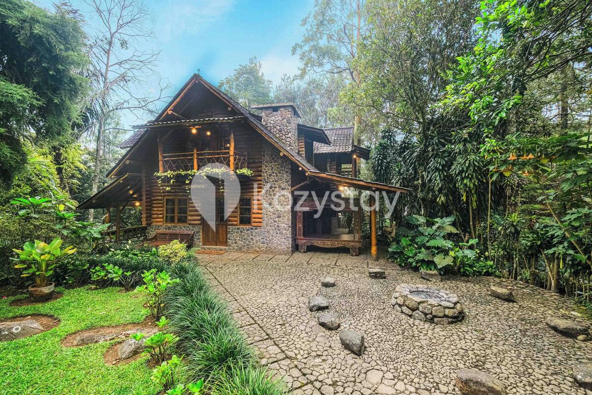 A rustic log cabin with a stone chimney, surrounded by lush greenery and a stone pathway leading to the entrance.