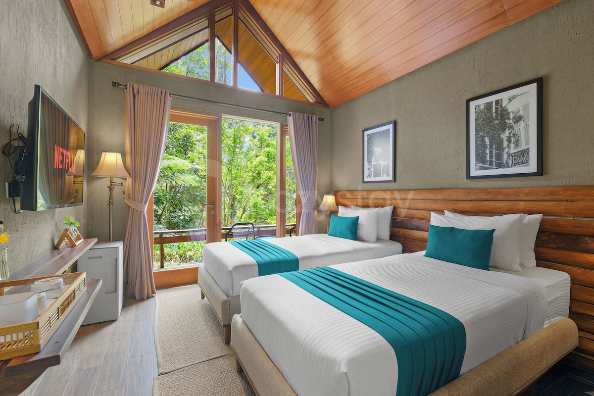 A hotel room with two beds, a TV, a desk, and a window with curtains.