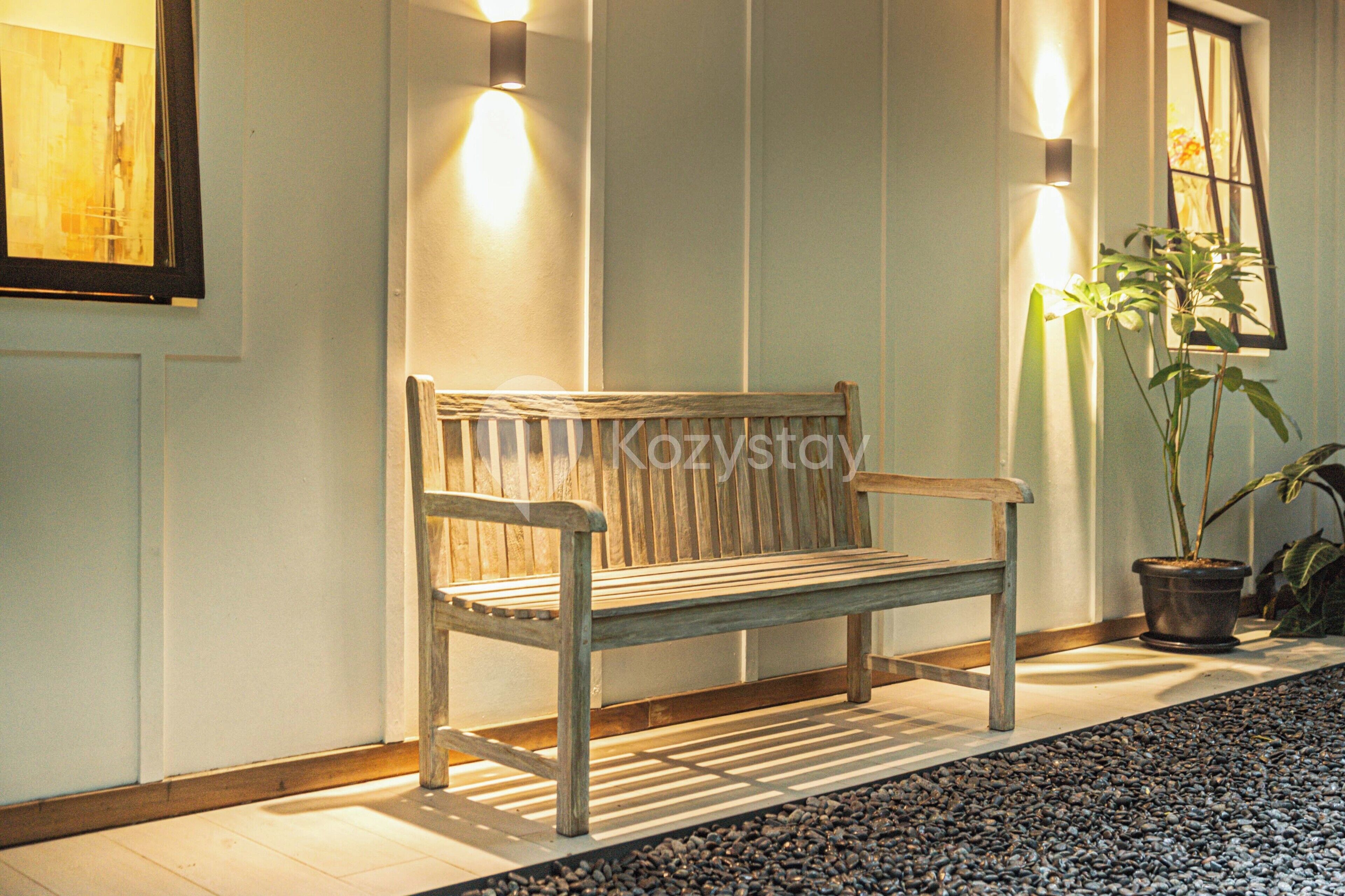 A wooden bench in a hallway with a potted plant and wall-mounted lights.
