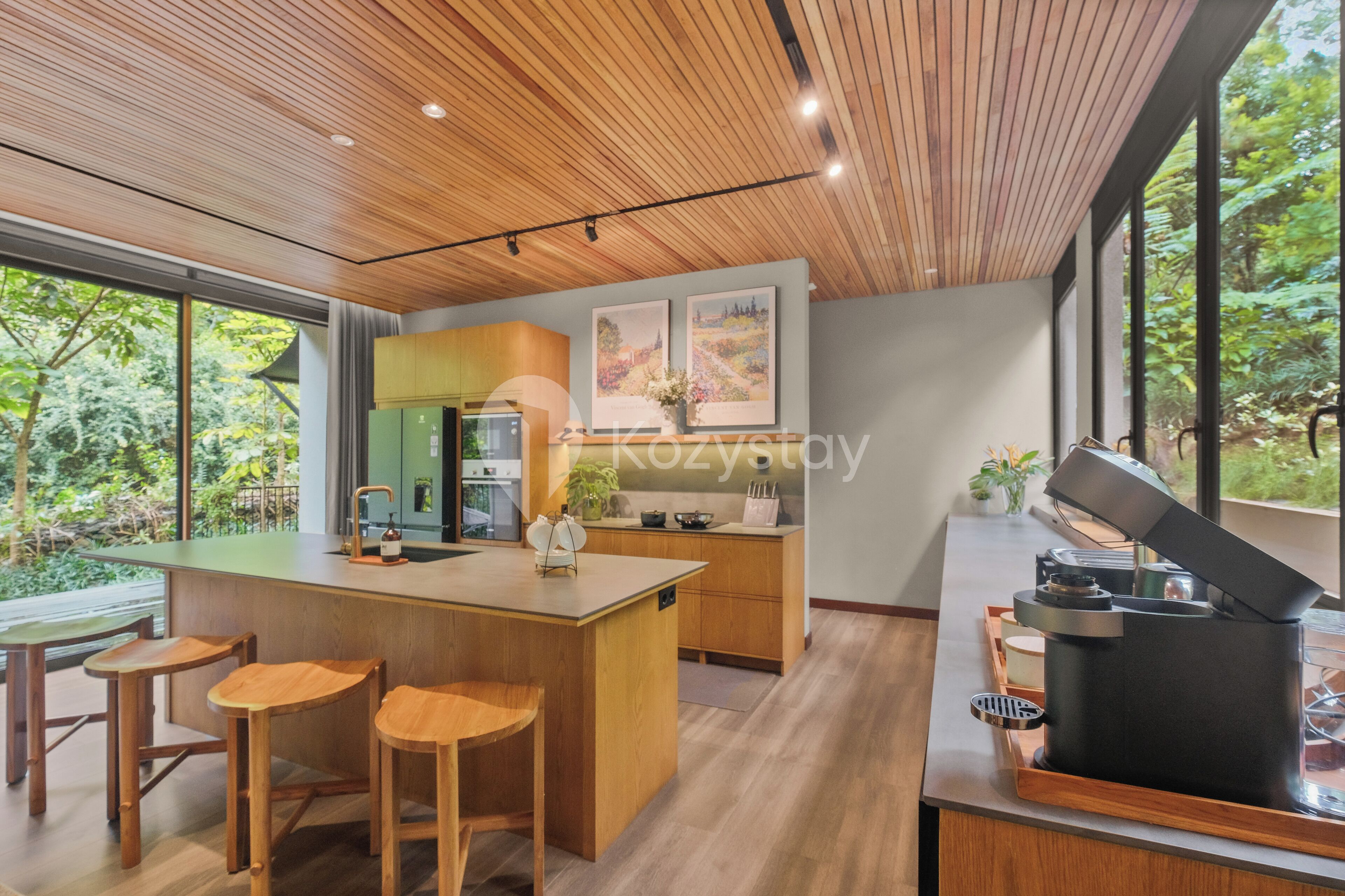A modern kitchen with wooden cabinetry, a central island with stools, and a coffee machine.