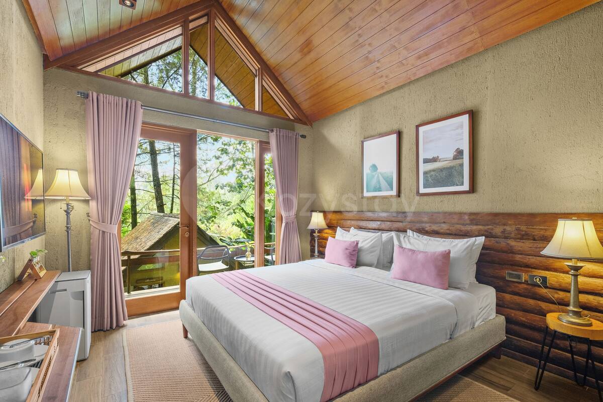 A bedroom with a large bed, a desk, a chair, and a window overlooking greenery.