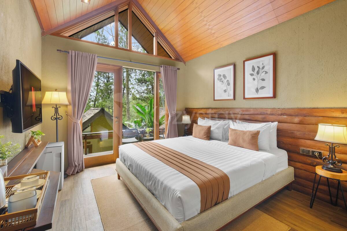 A bedroom with a large bed, a TV, a desk with a lamp, and a window with curtains.