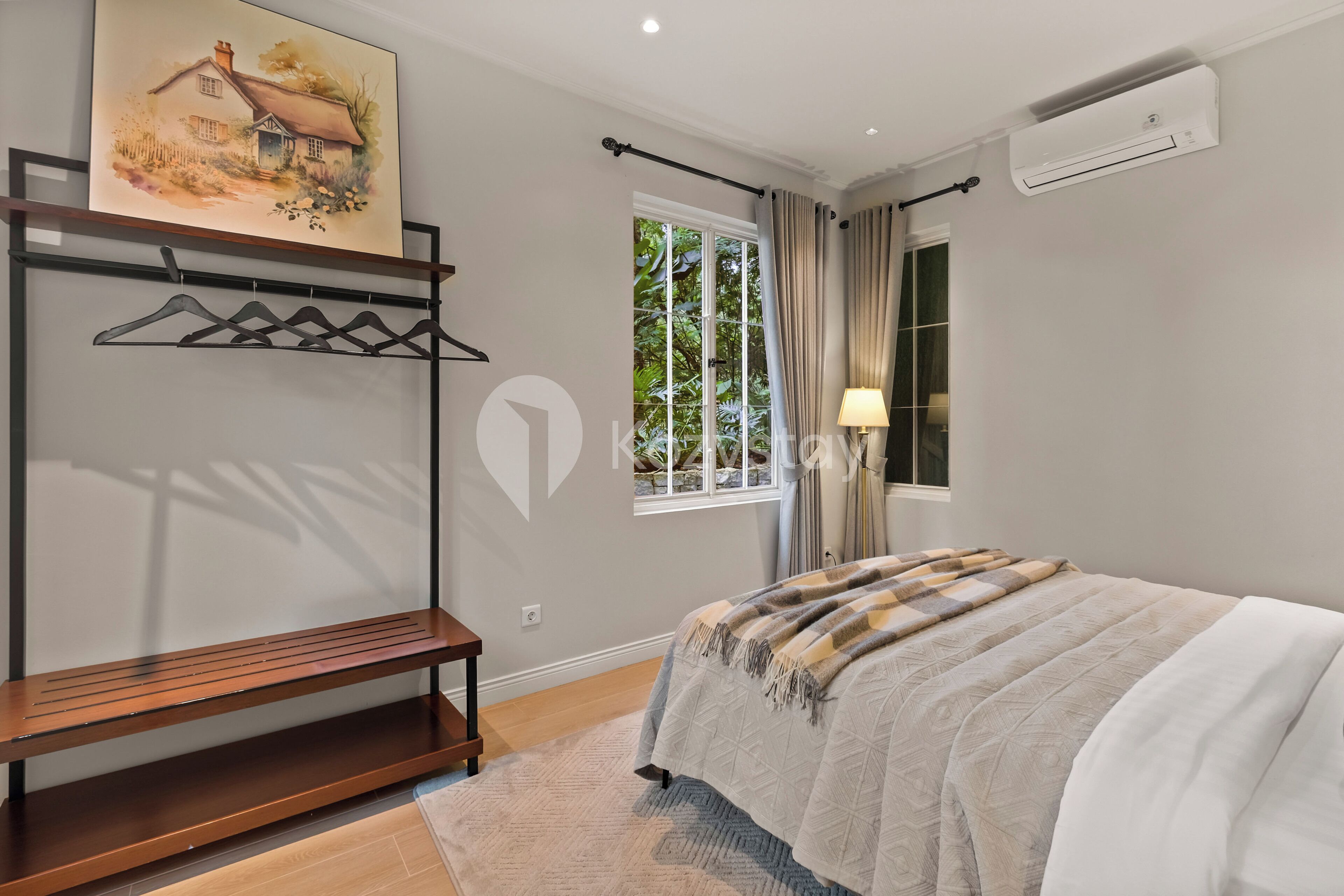 Une chambre à coucher avec un lit, un banc, un tableau, un climatiseur et une fenêtre avec des rideaux.
