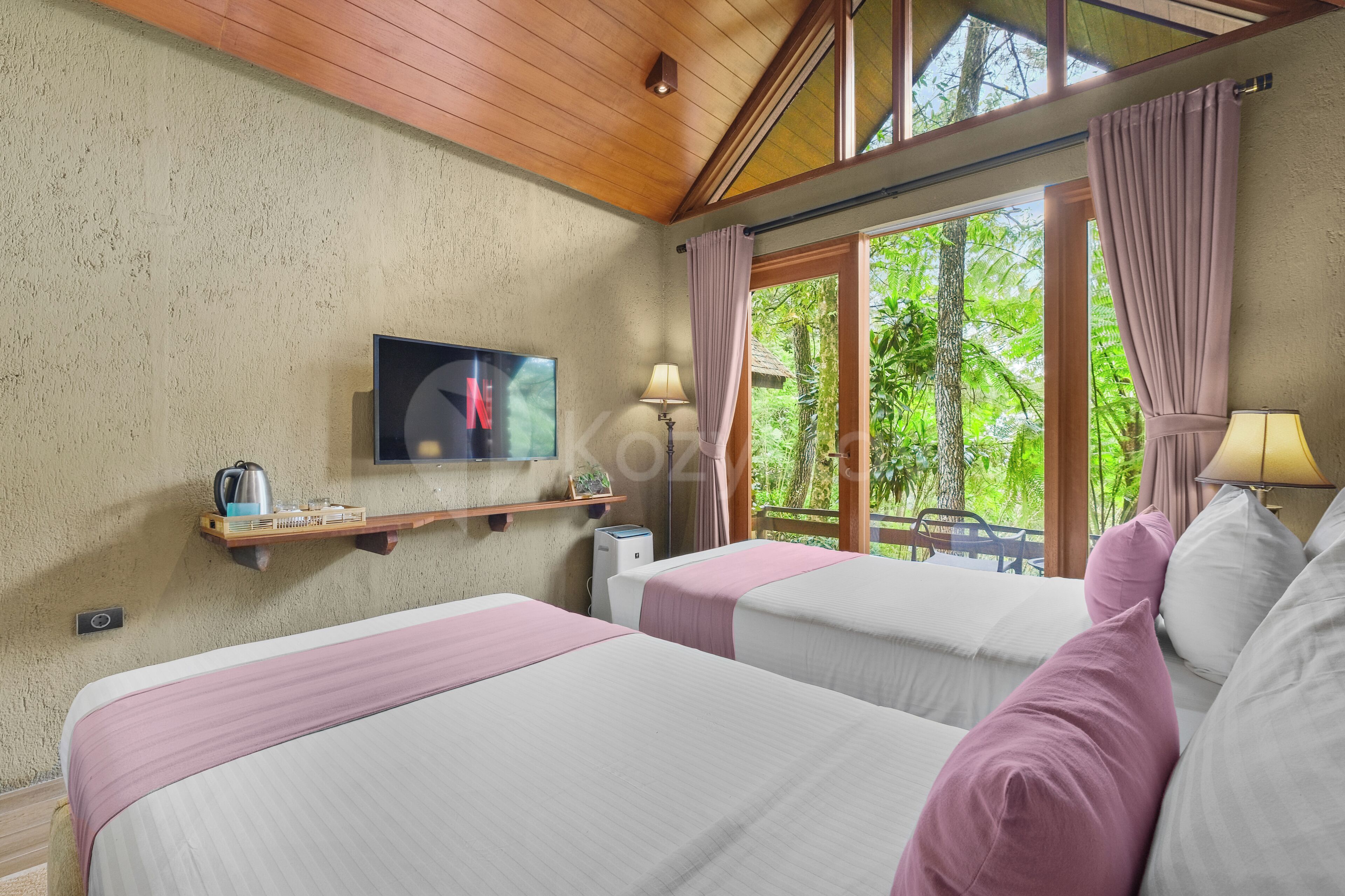 Une chambre d’hôtel avec deux lits, une télévision, une étagère avec une bouilloire et une fenêtre avec des rideaux.