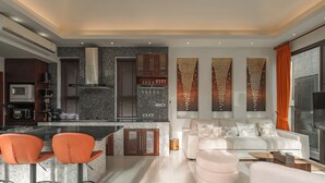 A modern kitchen with a central island, bar stools, a white sofa, and decorative wall panels. - PoolVilla Jacuzzi & Mountain View V232 (Rawai)
