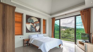 A bedroom with a large bed, a TV, and a view of a green landscape. - PoolVilla Jacuzzi & Mountain View V232 (Rawai)